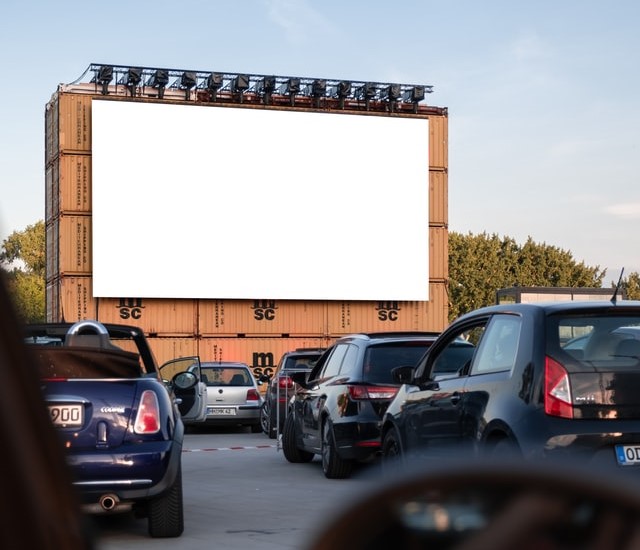 cinema drive-in, ao ar livre, com tela branca para projeção e carros enfileirados